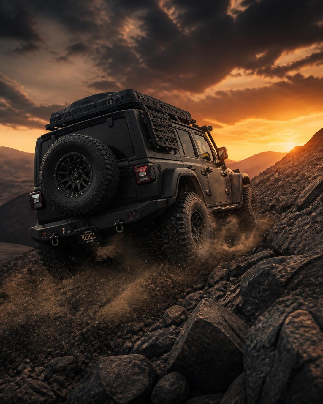 Jeep Rubicon modificado em preto fosco subindo uma crista rochosa ao pôr do sol